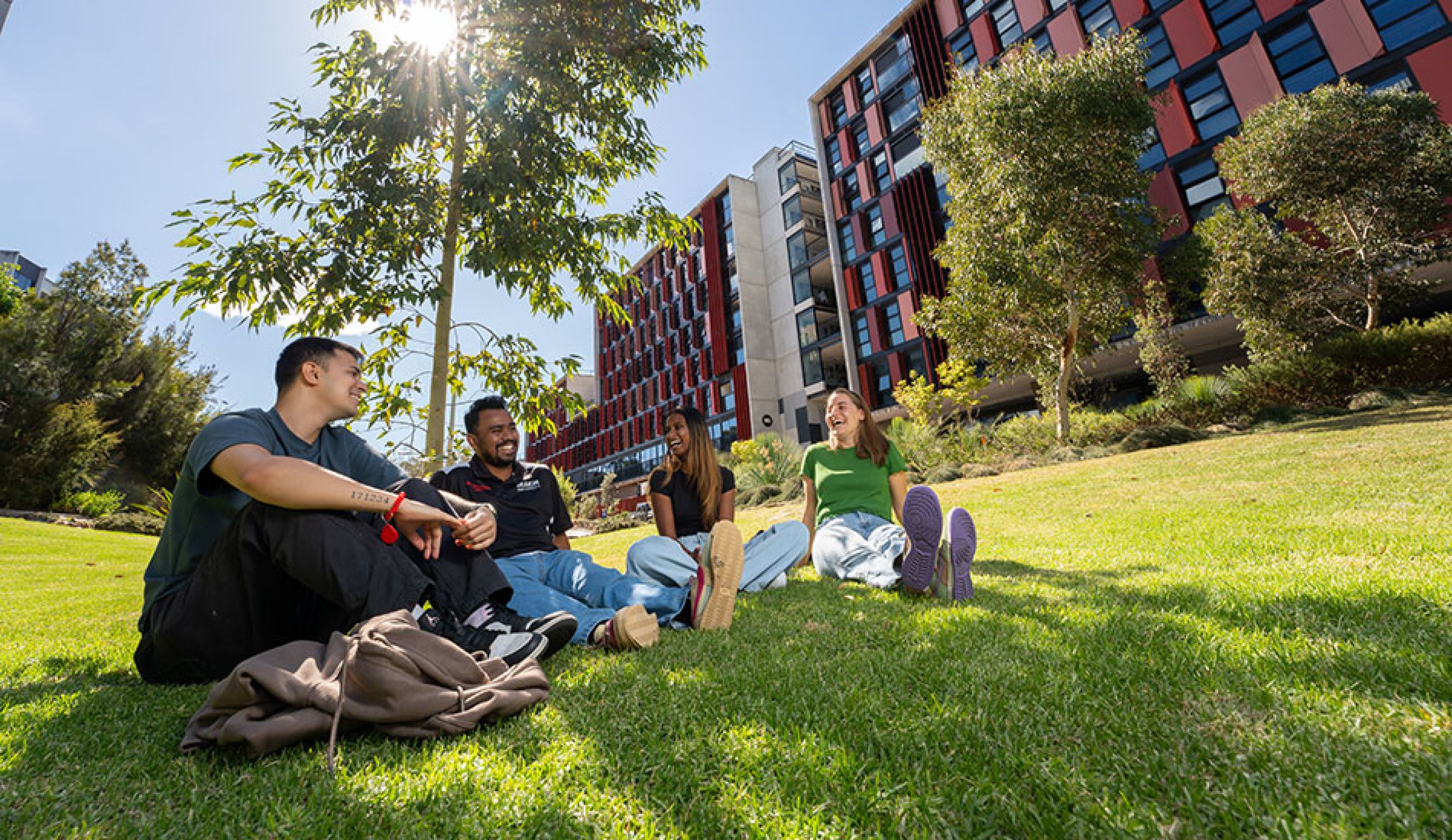 4 residents sitting on the grass with on-campus accommodation in background