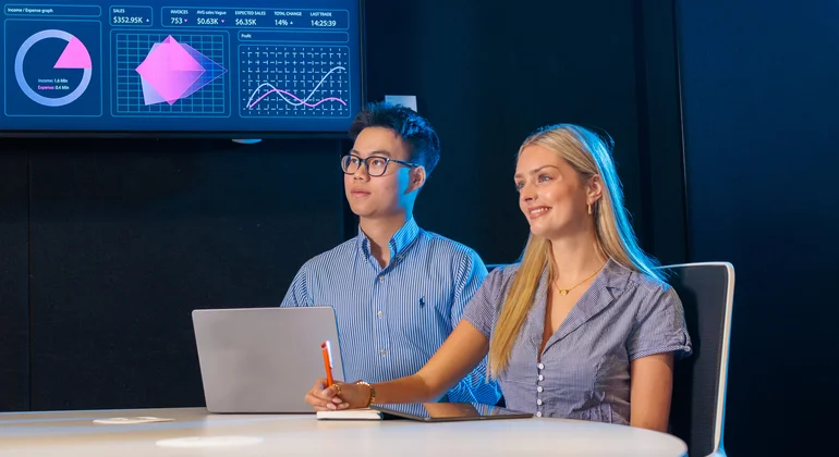 Two students reviewing data on a large screen.