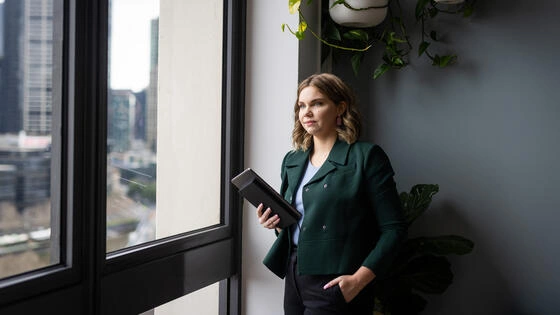 A Deakin business student stands looking out of a window holding a tablet