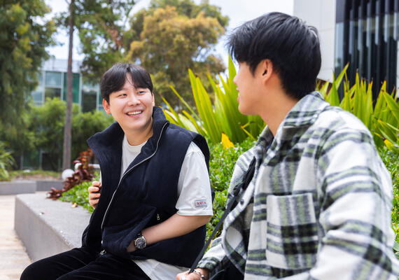 two international students sit on a ledge socialising 