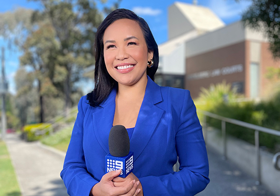 Deakin alum Neary Ty standing on footpath holding a microphone.