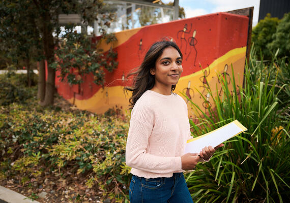 Confident female student walks past a mural.