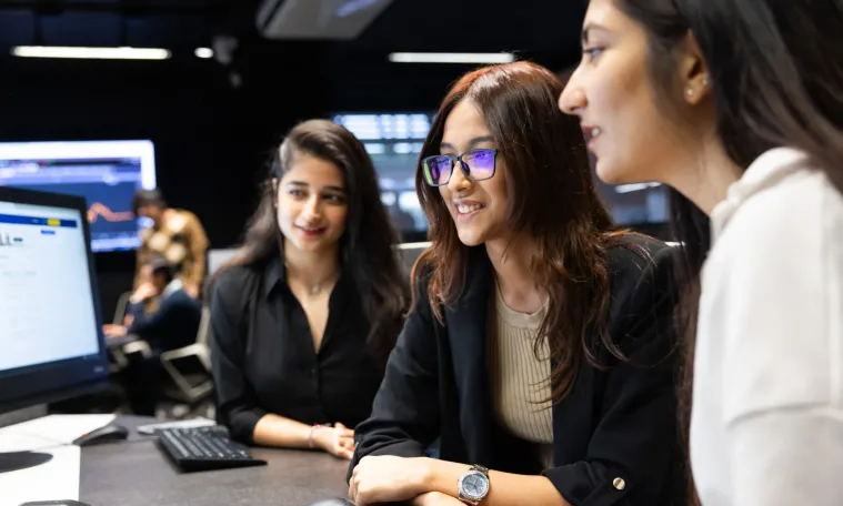 Three students look towards a computer