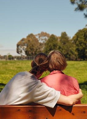 Two people embrace on a park bench outdoors.