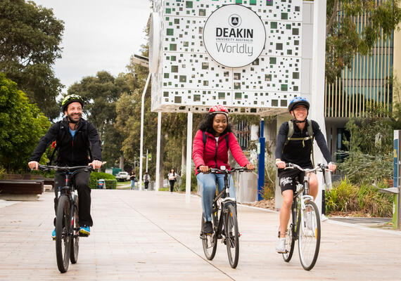 Three students ride bikes at the Deakin Burwood Campus.