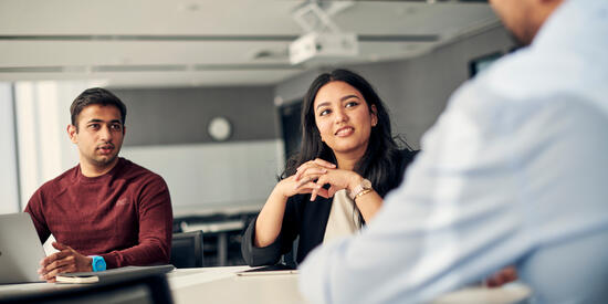 Three people sitting inside a boardroom and collaborating.