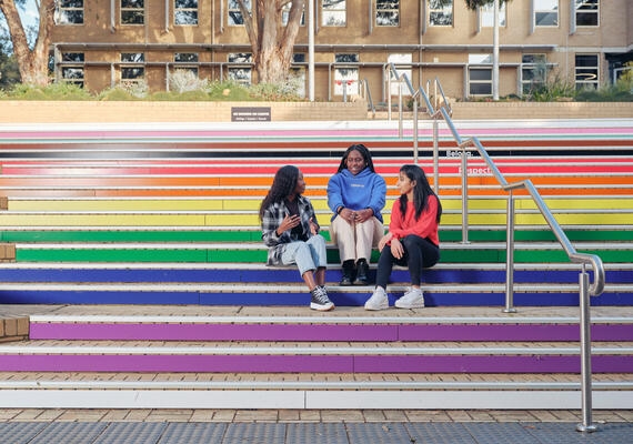 Three students sit on rainbow steps.