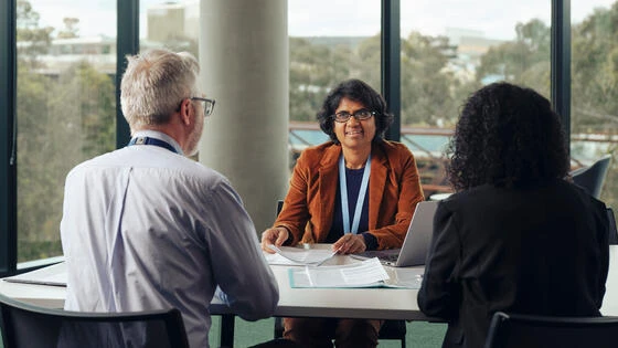 Three Deakin postgraduate health research practice students sit at a table chatting.