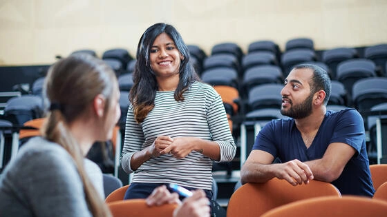 Three postgraduate education students talking in a lecture theatre.