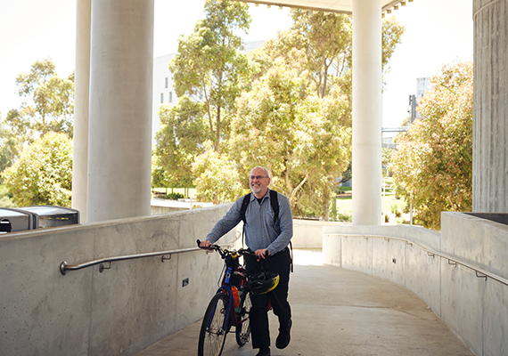 An older adult walking their bicycle up a walkway