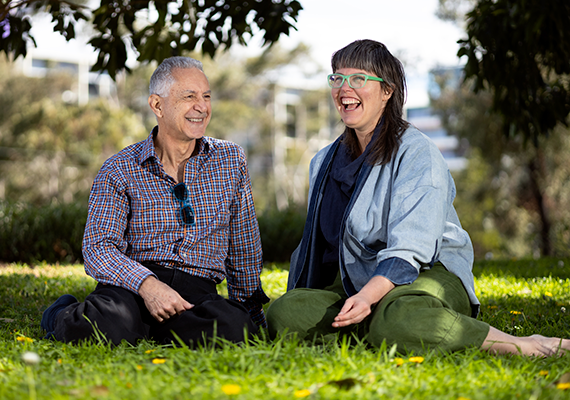 Dr Louisa Smith and Dr Dino Hodge sitting next to each other in a park looking at the camera. 