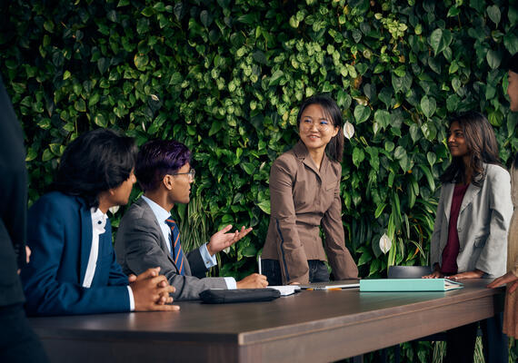 Female student wearing a business suit stands in a meeting.