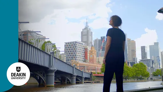 A Deakin arts and cultural management student standing outside in Melbourne and looking up at a bridge.