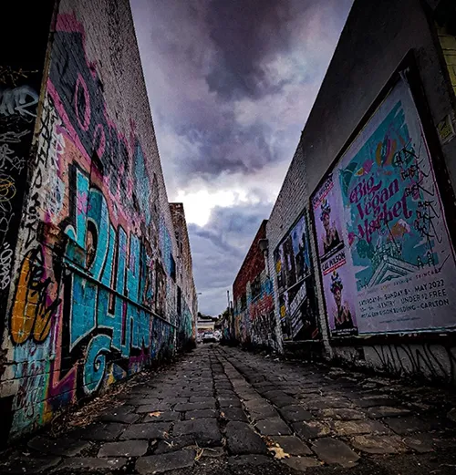 2022_Who_Am_I.webp A photo of an alley with bluestone cobbles and grafitti covered brick walls