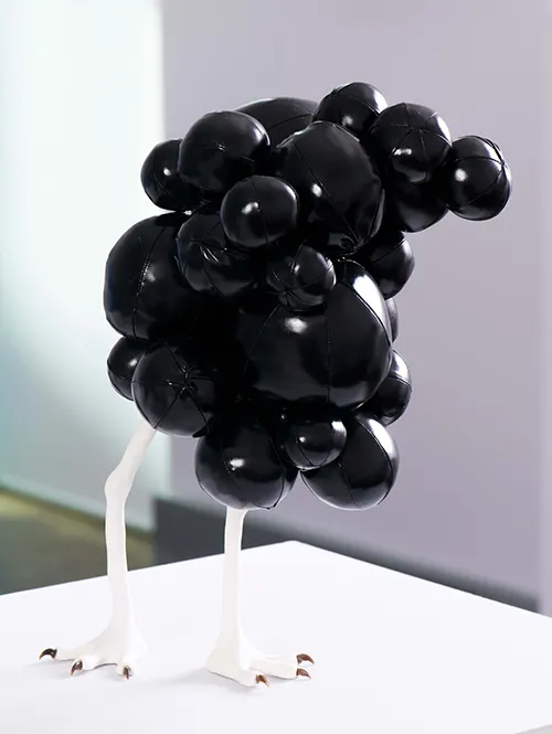 Sculpture of a bunch of small black balloons on white legs with claws