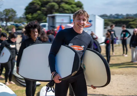 A Deakin exchange and study abroad student carrying a surf board on the beach.
