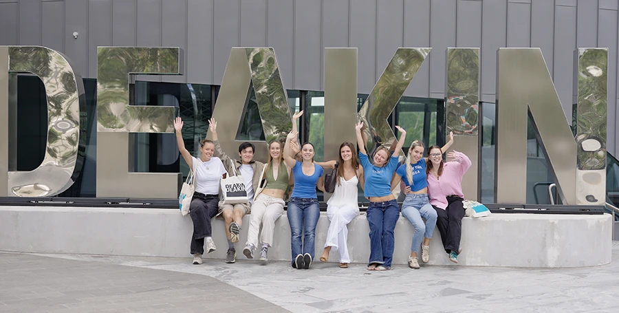 International Summer School students sitting in front of the Deakin University sign at Melbourne Burwood Campus.