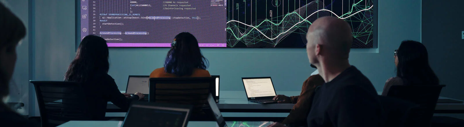 Deakin postgraduate data analytics students discussing and analysing data in classroom with projection on large wall screen.