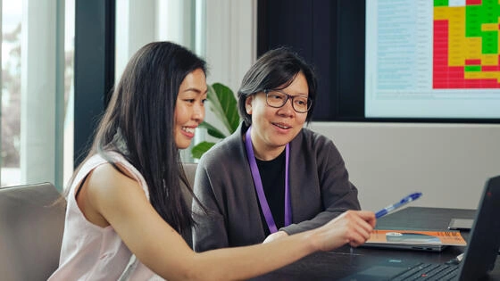 Two Deakin postgraduate health promotion students look at a laptop.