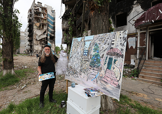 Artist George Gittoes painting at an easel in front of a dilapidated building