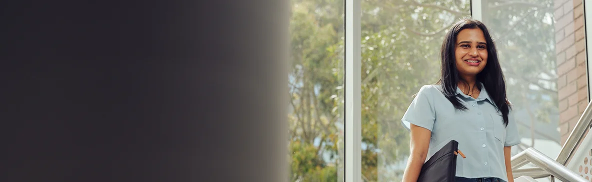 A smiling postgraduate student walks down stairs on the Burwood campus.