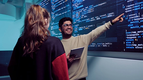 Two Deakin IT student talk with a screen of data behind them. 