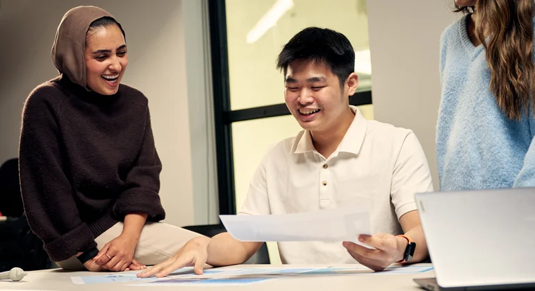 Three postgraduate communication students talking at desk.