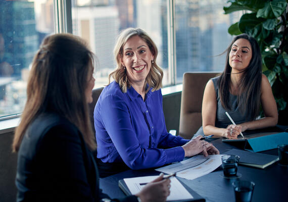 Three MBA students sit at a desk studying in a city building.