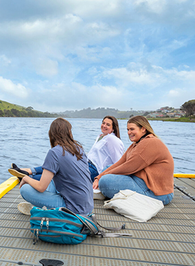 Three Deakin international students socialise while sitting on a jetty