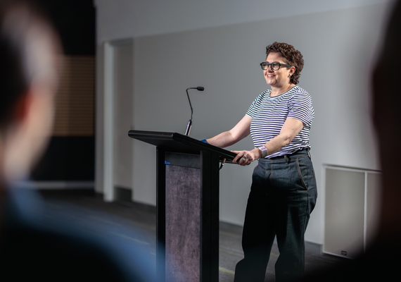 A person wearing a striped shirt stands behind a podium and gives a presentation.