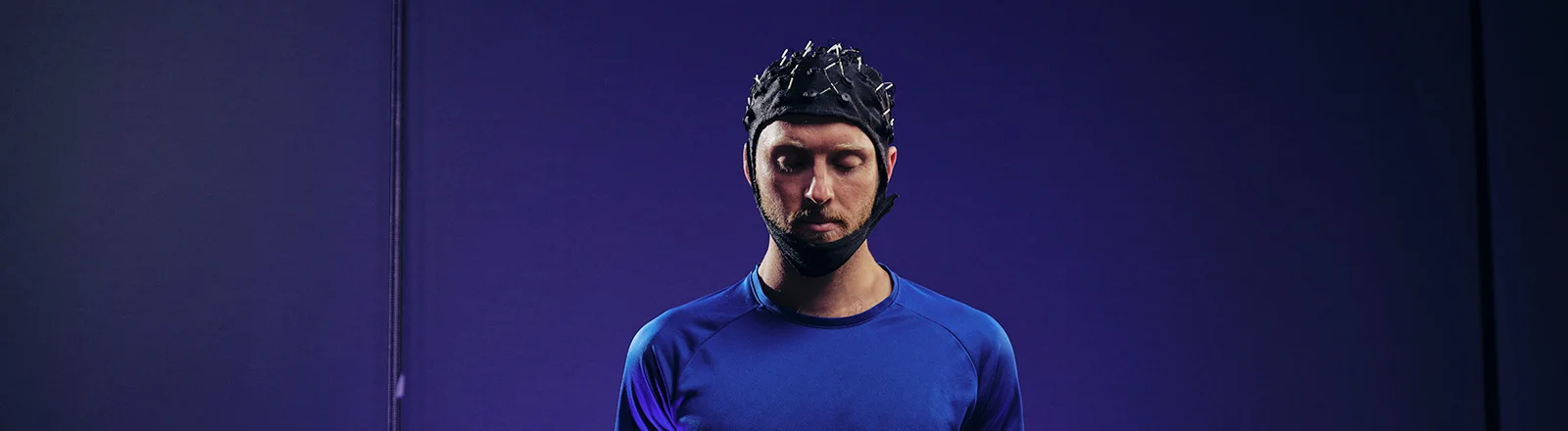 A psychology student wears helmet standing in a blue room.