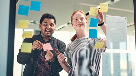 Two Deakin postgraduate information systems students put sticky notes on a glass door.