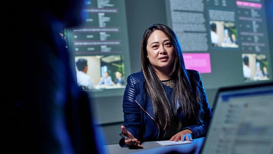 A Deakin postgraduate marketing technology student inside classroom with data graphs on a presentation screen.