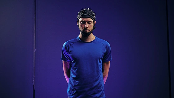 A Deakin psychology student wears a helmet standing in a blue room.