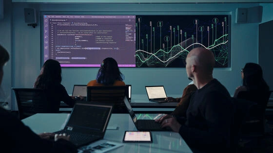 Deakin postgraduate data analytics students discussing and analysing data in classroom with projection on large wall screen.